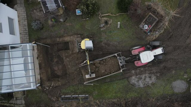 aerial drone shot of yellow excavator stands in a large garden and digs a hole for a pool in austria