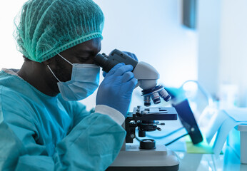 Scientist working in laboratory examining coronavirus through microscope - Science and technology...