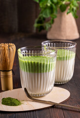 Matcha green latte tea with matcha powder and bamboo whisk on wood background.