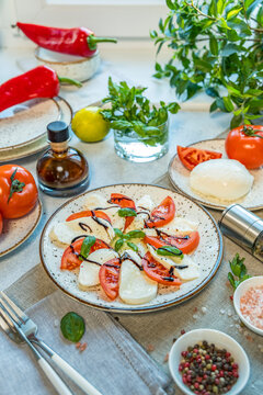 Caprese salad with sliced fresh tomatoes, mozzarella cheese and basil served on a white plate on light gray table surface.