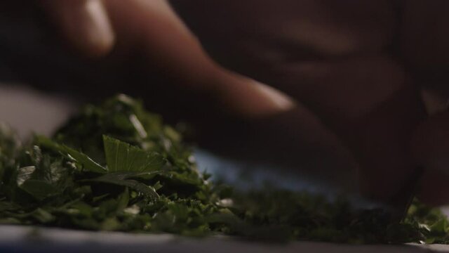 French chef is chopping parsley on a cutting board in slow motion. Chopping vegetables in gastronomic restaurant. 