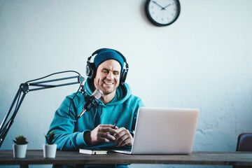 Cheerful host streaming his audio podcast at small and cozy home broadcast studio