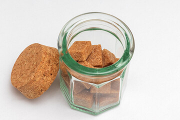 Glass cup with brown sugar cubes and cork top lid against white background topview.