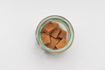 Glass cup with brown sugar cubes and cork top lid against white background seen from top.