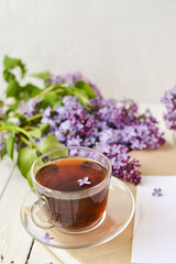 Romantic background with a cup of tea, lilac flowers and a book over a white wooden table. Leisure concept, spring breakfast