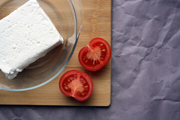 Cottage cheese in a bowl on a wooden board and tomato.