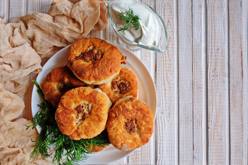Homemade fried dough with minced meat or belyashi. Pies are on a plate on a white wooden table. Top view. Copy space.