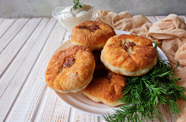 Homemade fried dough with minced meat or belyashi. Pies are on a plate on a white wooden table. Copy space.