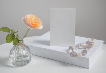 Beautiful rose flower in glass vase with mock up  invitation card and white book decoration with Amethyst and Quartz necklace on white table background