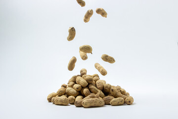 Peanuts on a white background. A peanut falls on a pile of peanuts. Peanuts in shell