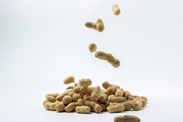 Peanuts on a white background. A peanut falls on a pile of peanuts. Peanuts in shell