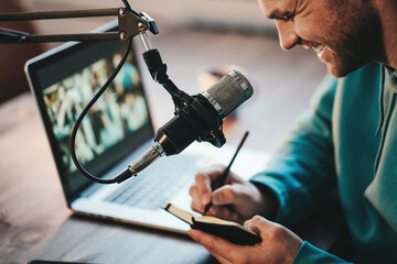 Cheerful host streaming his audio podcast using microphone and laptop at his small broadcast studio