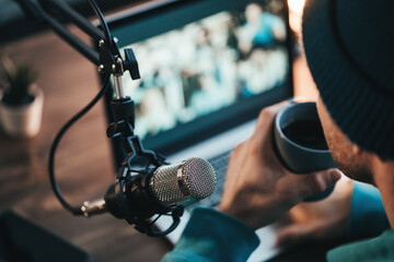 A man host streaming his audio podcast using microphone and laptop at his small broadcast studio,...