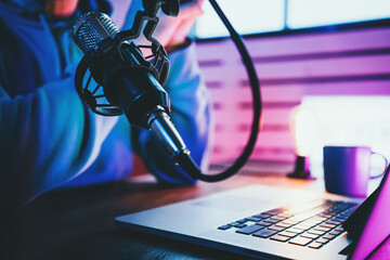 Trendy podcast creator streaming audio broadcast at his home studio using stylish cyber punk...