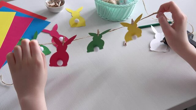 Boy made Easter paper garland. Multicolored Easter bunnies made of paper and pompons on string with clothespins