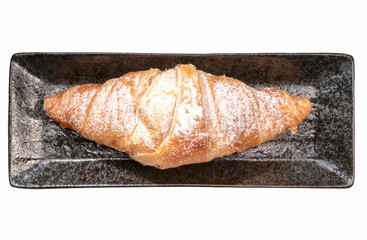 Croissant with powdered sugar on black plate on white background.