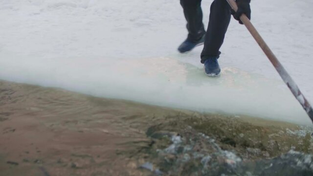 Man walks near ice hole and removes thin layer of ice from water.