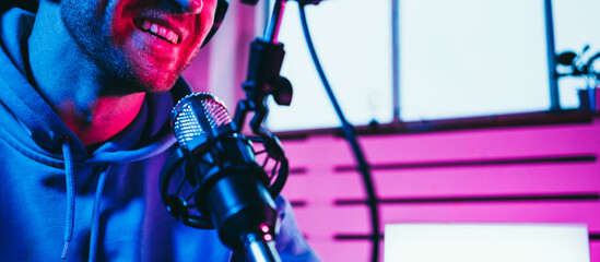 Cheerful streamer  broadcasting his audio show at home studio using stylish cyber punk blue magenta...