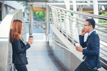 Businessman Businesswoman drinking coffee in town using smartphone outside office modern city. Hands holding take away coffee cup and smart phone talking together Business partner with cup of coffee