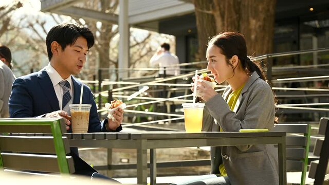 カフェのテラス席でランチをする会社員の男女	
