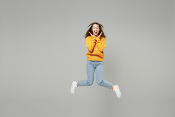 Fototapeta na wymiar Full length of young excited overjoyed surprised shocked woman in knitted yellow sweater in air jump high with outstretched hands legs spreading hands isolated on grey background studio portrait