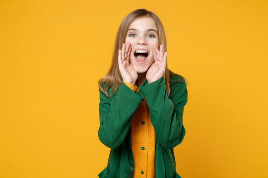 Little blonde curious secret kid girl 12-13 years old wearing casual clothes green shirt scream news with hands near mouth isolated on yellow orange background children studio. Childhood concept..