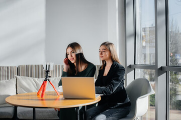 Two young beautiful girls are sitting in a cafe, recording video blogs and communicating on social networks.