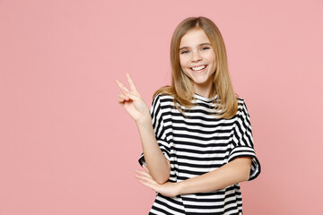 Little blonde smiling cute kid nice girl 12-13 years old wearing striped oversized t-shirt show victory v-sign gesture isolated on pastel pink background children studio . Childhood lifestyle concept.