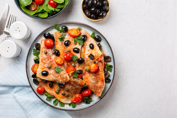 Italian lunch. Perch fish fillets stew, italian style, with black olives, tomatoes, capers, fresh parsley.  Fresh salad. Light grey background. Top view. Copy space.