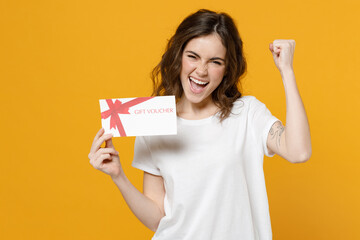 Young happy overjoyed fun caucasian woman in white basic t-shirt point index finger on gift voucher...