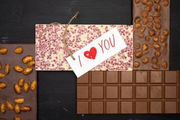 some different sweet bars of chocolate lie on a black wooden background with a label that says I love you