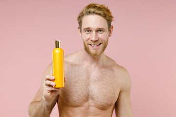Smiling handsome bearded naked young man 20s perfect skin hold empty blank bottle of shampoo...