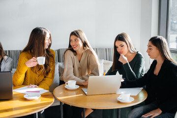 A group of young girls sit in an office at computers and discuss projects. Communication and training online.