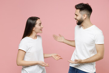 Young cheerful couple two friends bearded man brunette woman in white basic blank print design t-shirts standing smiling talking to each other telling stories isolated on pastel pink color background.