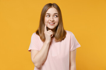 Young smiling dreamful wistful positive student woman 20s with nude make up wearing casual basic pastel pink t-shirt looking aside prop up face isolated on yellow color background studio portrait