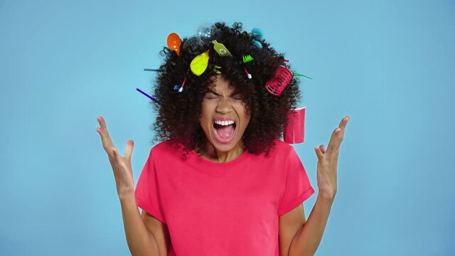 Screaming and agry afro american woman with plastic trash in the curly hair.