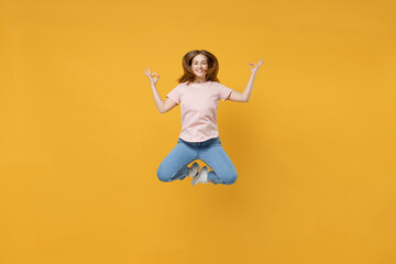 Obraz premium Full length of young overjoyed energetic excited woman 20s wearing casual basic pastel pink t-shirt jumping high hold hands in yoga gesture, meditating isolated on yellow background studio portrait.