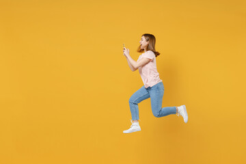 Fototapeta na wymiar Full length side profeli view of young expressive excited overjoyed woman 20s in basic pastel pink t-shirt jump high run holding mobile cell phone using fast internet isolated on yellow background .