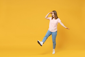 Full length of young caucasian woman 20s with nude make up in casual basic pastel pink t-shirt, jeans holding hand at forehead looking far away distance isolated on yellow background studio portrait.