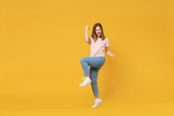 Full length of young caucasian overjoyed excited woman 20s in basic pastel pink t-shirt, jeans do winner gesture clench fist celebrating, raised up leg isolated on yellow background studio portrait.