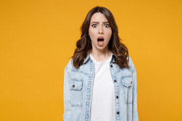 Young shocked confused wondered astonished indignant woman 20s wearing stylish casual denim shirt white t-shirt looking camera with opened mouth isolated on yellow color background studio portrait