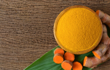  Turmeric powder in a wooden bowl and turmeric (curcumin) rhizome on wooden background,Top view,copy space.