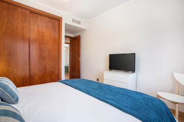 Shot from corner of bedroom, view from bed to a tv on a stand, a wardrobe on the side and an open...