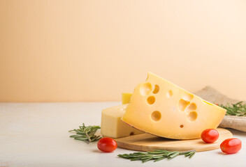 Various types of cheese with rosemary and tomatoes on wooden board on a white and orange background. Side view, copy space.