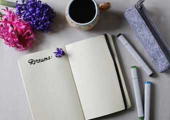 Opened notebook moleskin with blank pages to write dreams and plans on linen background with a cup of black coffee and purple and pink hyacinths blooming. Lifestyle top view flat lay. 