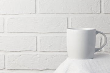 Household utensils, a white cup stands on a napkin against the background of a kitchen stone brick wall of a milky shade, the concept of clean dishes