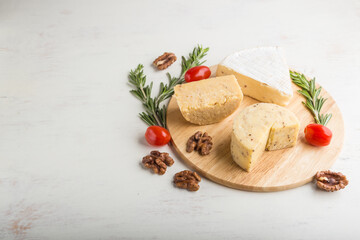 Fototapeta na wymiar Cheddar and various types of cheese with rosemary and tomatoes on wooden board on a white background . Side view, copy space.