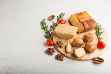 Smoked cheese and various types of cheese with rosemary and tomatoes on wooden board on a white background. Side view, copy space.