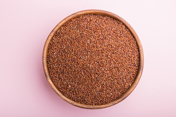 Wooden bowl with raw red quinoa seeds on a pastel pink background.  Top view, close up.