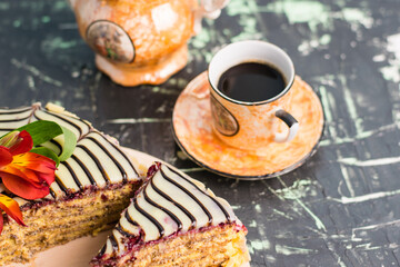 Espresso coffee in a cup and a slice of delicious cake with cream, almonds, white and dark chocolate on the table